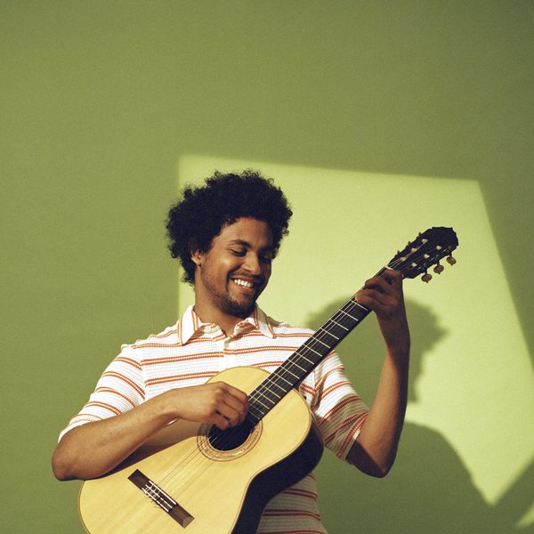 Plinio Fernandes plays guitar, smiling.
