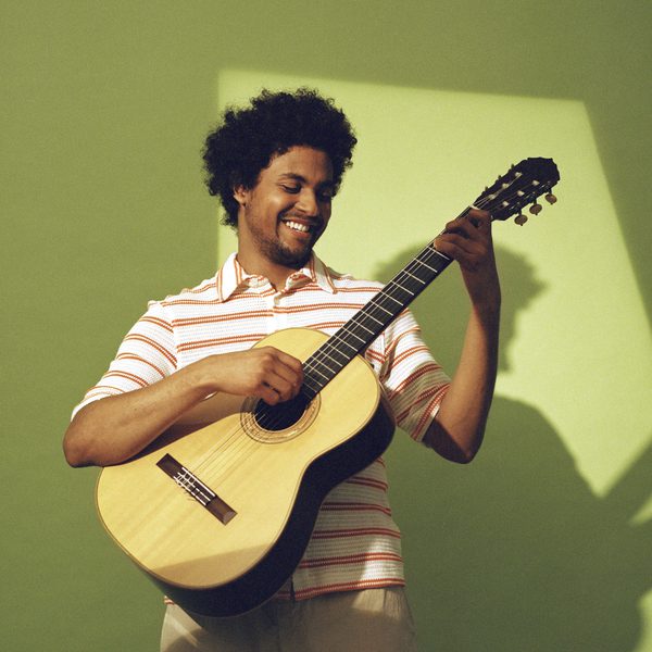 Plinio Fernandes plays guitar, smiling.