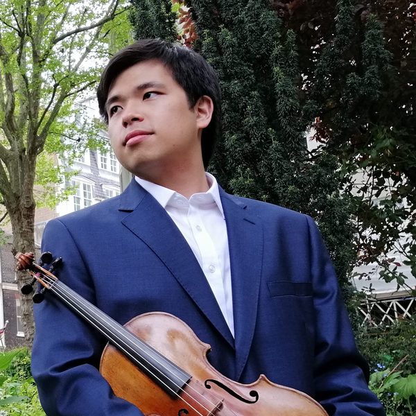Preston Yeo holds a violin at waist level outdoors, looking out of frame.