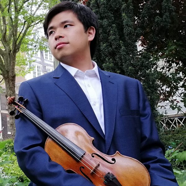 Preston Yeo holds a violin at waist level outdoors, looking out of frame.