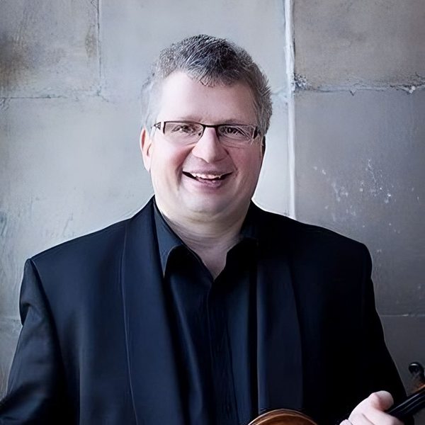 Rafael Todes poses for camera outside, holding a violin at chest with both hands.