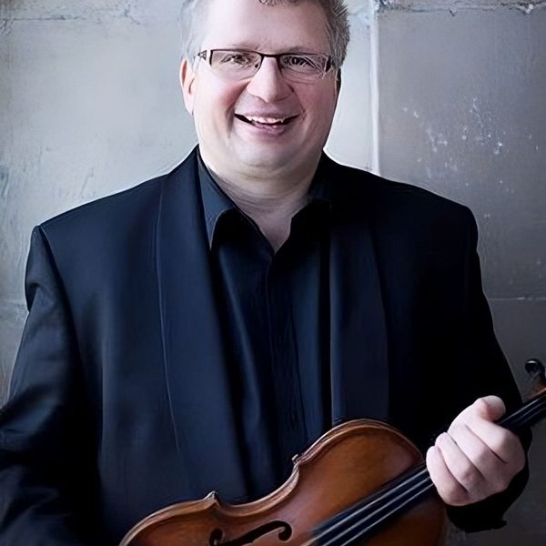 Rafael Todes poses for camera outside, holding a violin at chest with both hands.