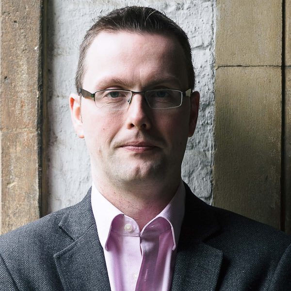 Portrait of Richard Pinel looking to camera, standing against a brick wall.