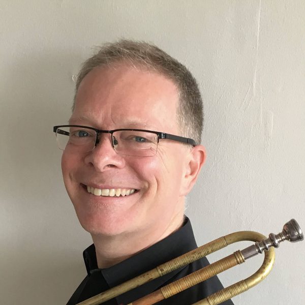 Robert farley smiles to camera, with a brass instrument slung over shoulder.