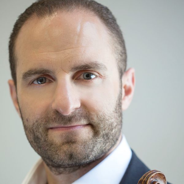 Portrait of Robin Wilson looking to camera, holding violin against chest.