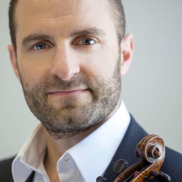 Portrait of Robin Wilson looking to camera, holding violin against chest.