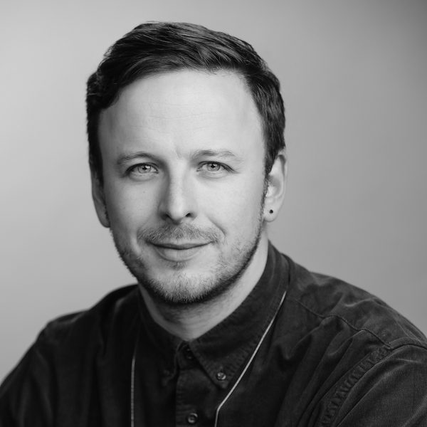Samuel Queen smiles to camera in a greyscale headshot.