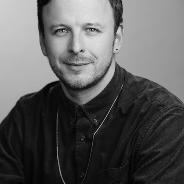 Samuel Queen smiles to camera in a greyscale headshot.