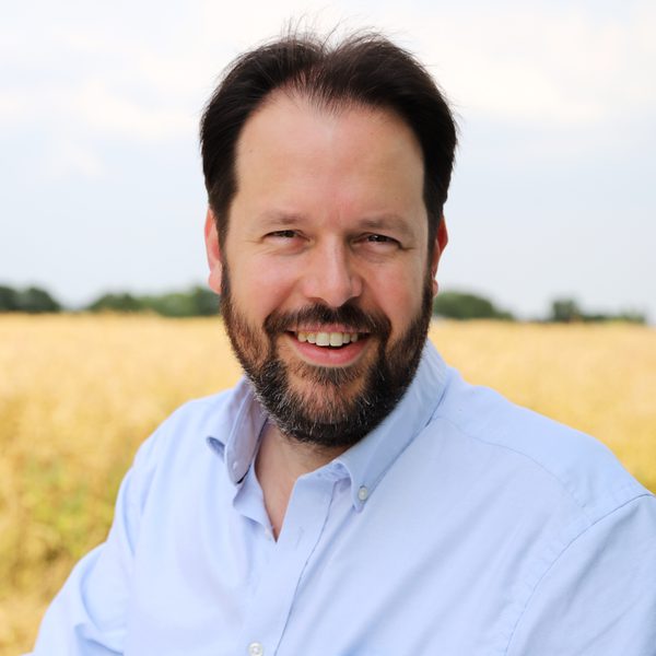 Portrait of Sholto Kynoch smiling to camera against a rural background.