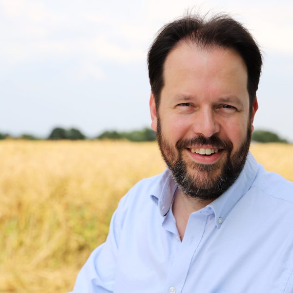 Portrait of Sholto Kynoch smiling to camera against a rural background.