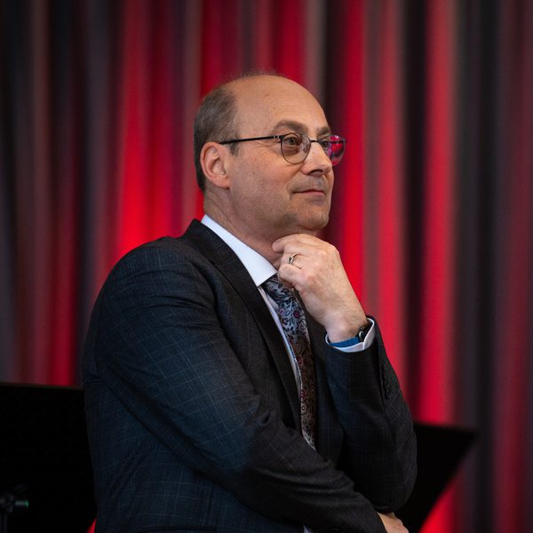 Simon Carr sits in profile in front of a red curtain, with arms folded and hand under chin.
