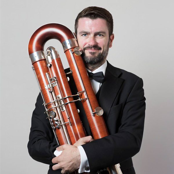 Simon Estell smiles to camera, holding bassoon.