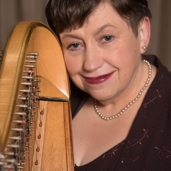 Sioned Williams smiling, holding a harp column.