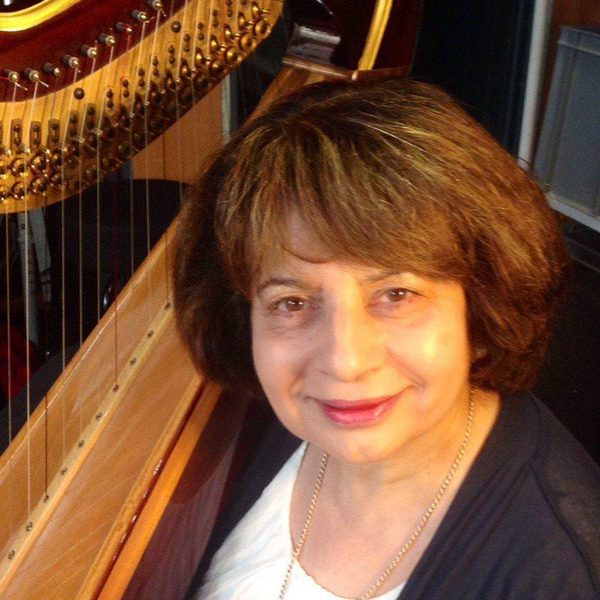 Skaila Kanga smiles to camera, standing next to a harp.