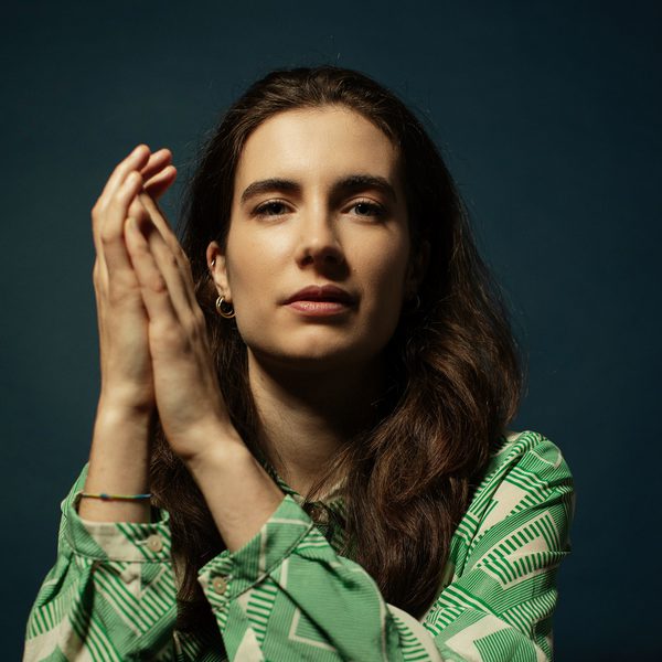 Portrait of Sofia Sacco leaning over the back of a chair, facing camera, clasping hands together.