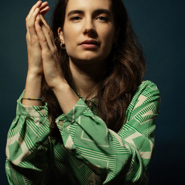 Portrait of Sofia Sacco leaning over the back of a chair, facing camera, clasping hands together.