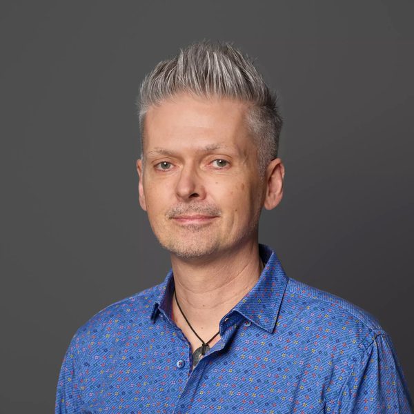 Stephen Fitzpatrick smiles to camera against a dark grey background.