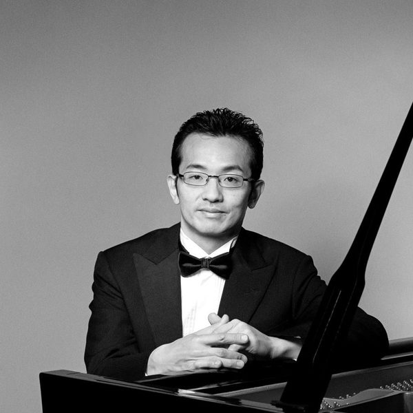 Tadashi Imai sits at a piano, smiling to camera.