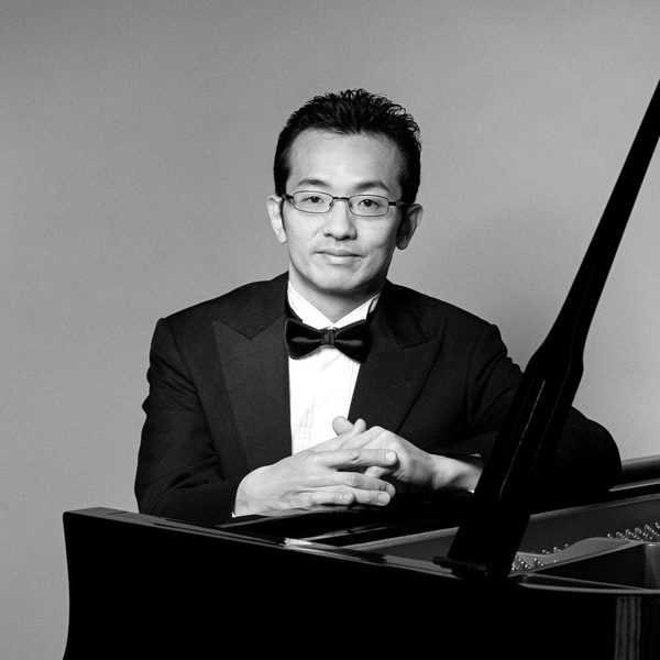 Tadashi Imai sits at a piano, smiling to camera.
