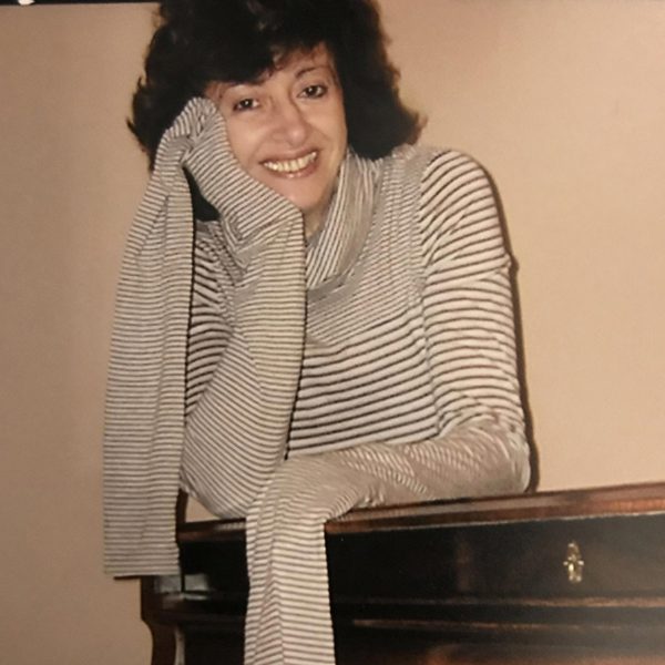Tatiana Sarkissova leans on a piano, smiling to camera.