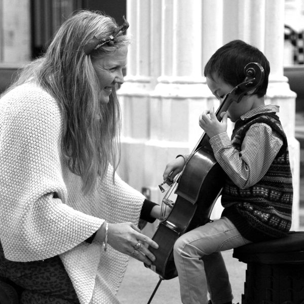 A smiling cello teacher attends to a very young cellist.