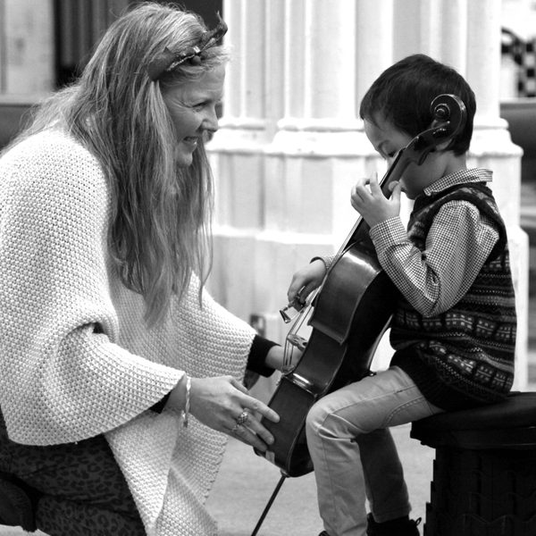 A smiling cello teacher attends to a very young cellist.
