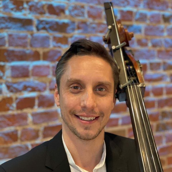 Thomas Goodman smiles to camera against a brick wall.