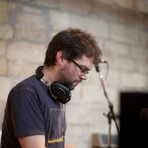 Side portrait of a pianist with hands on the keyboard and a microphone stand in the background.