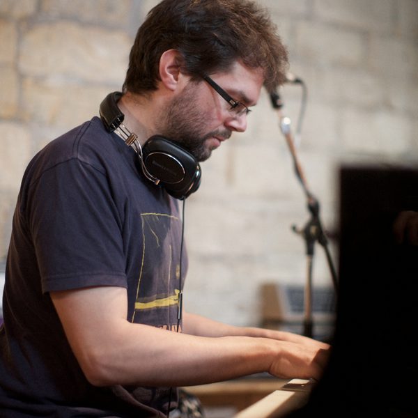 Side portrait of a pianist with hands on the keyboard and a microphone stand in the background.