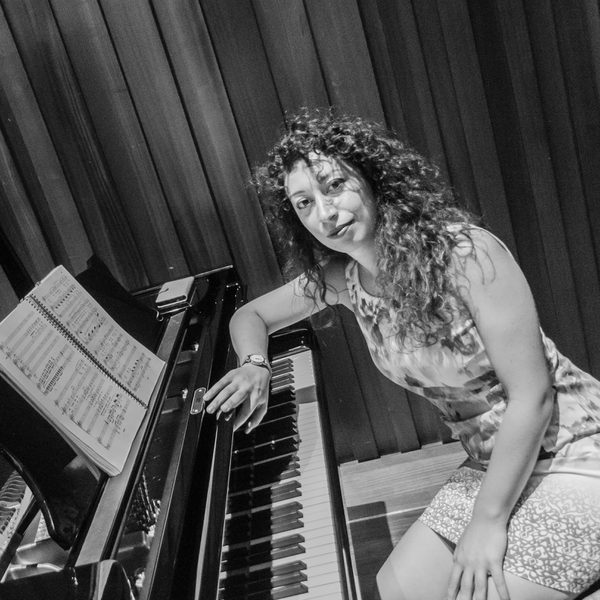 Valeria Racco sits at the piano and looks to camera.