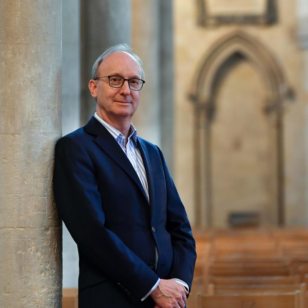 David Titterington smiles to camera with arms held in front, leaning against a church column